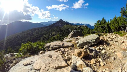 Majestic mountain vista from rocky peak, hiker's perspective. Sunlit landscape with panoramic view.
