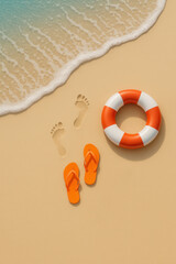 Naklejka premium An overhead view of a tranquil beach scene shows the shoreline with soft waves, a pair of orange flip-flops, distinct footprints in the sand, and a red-and-white lifebuoy placed nearby. 