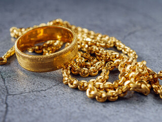 Gold price, gold jewelry, close-up of gold ring and gold necklace on grey background.