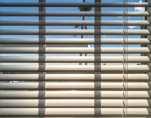 Sunlit beige window blinds partially open, revealing a clear blue sky.  Perfect for home decor, interior design, and architectural projects.