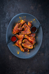 Authentical barbecue chicken wings and drumsticks with hot chili and grill sauce served as top view on a design plate