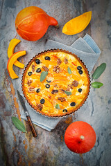 Homemade pumpkin savory tart quiche pastry with black olives, walnuts and fresh cheese served as top view in a baking form