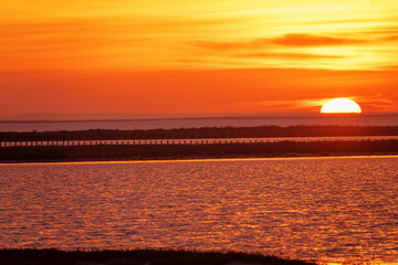 The disk of the sun sinks below the horizon, the last seconds of sunset over the lake