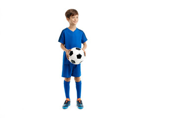 Confident young boy in blue sport outfit posing with classic soccer ball over white background