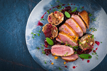 Roasted duck breast filet with homemade bread mushroom dumplings, orange topping and herbs served with cranberry sauce as top view on a design plate