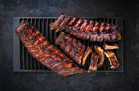 Charcoal smoked barbecue spareribs St Louis cut with hot rub and BBQ sauce served as top view on an old rustic grillage