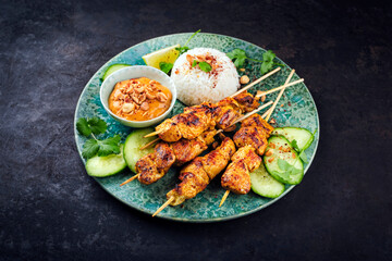 Sate Ayam- Grilled chicken satay sate skewers with peanut dipping spicy sauce, steamed rice and fresh cucumber served as close-up on a design plate