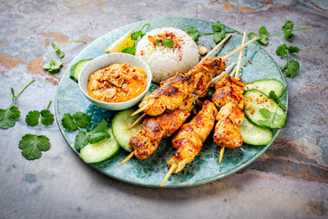 Sate ayam- grilled chicken satay sate skewers with peanut dipping spicy sauce, steamed rice and fresh cucumber served as close-up on a design plate