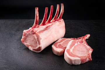 Raw dry aged bone-in back rack of pork loin offered as close-up on a black board