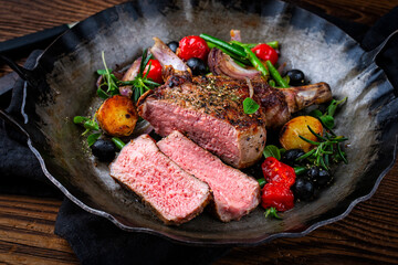 Traditional barbecue dry aged veal chop Mediterranean vegetable and fried potatoes served as close-up in a rustic cast iron frying pan on a wooden table