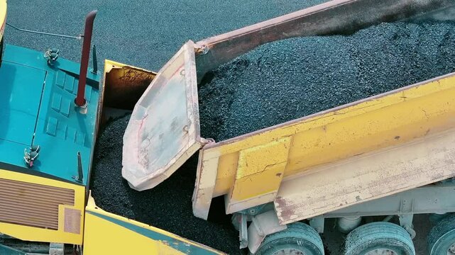 Truck pouring asphalt into asphalt machine