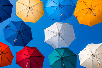 Multicolored umbrellas create a vibrant canopy over the lively street in a sunny neighborhood