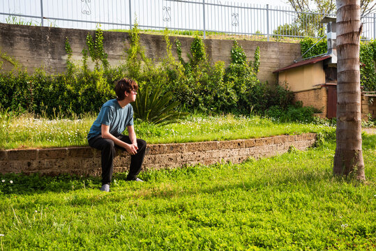 Caucasian teenage boy of 16-17 year old sitting outdoors in summer