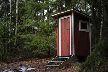 Scandinavian-style wooden toilet cabin painted in classic red, standing in the forest, Sipoonkorpi National Park, Finland