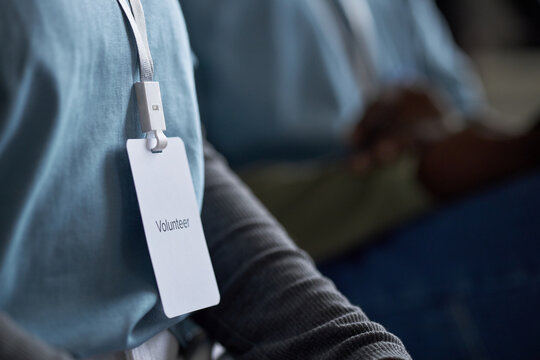Individual wearing laminated volunteer badge on lanyard during charity event. Close-up image showcasing name tag and professional environment background