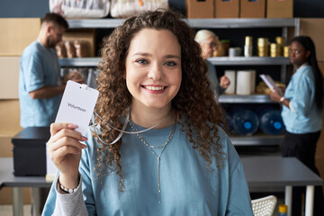 Portrait of young smiling female volunteer with curly hair, wearing blue shirt, holding...