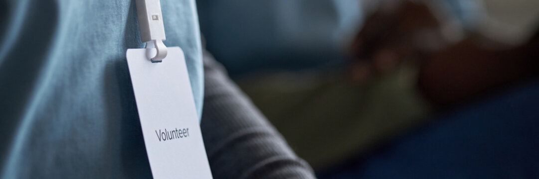 Close-up photo showing person wearing volunteer badge pinned to shirt sleeve during charity event. Background shows blurred people part of event