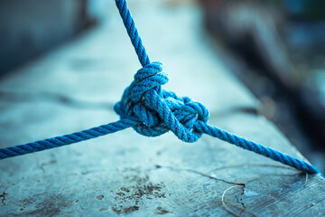 A detailed close-up of a blue rope tied in a strong knot against a textured concrete background. This image symbolizes connection, strength, reliability, teamwork, and resilience.