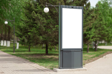An empty outdoor billboard on a background of green plants. An empty advertising banner, a frame. City sidewalk