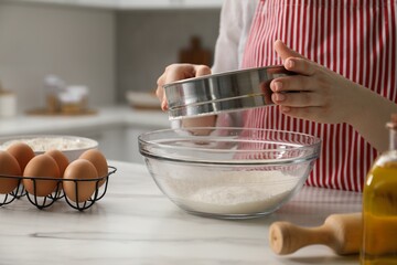 Making khinkali. Woman sieving flour into bowl at table in kitchen, closeup
