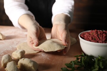 Making khinkali. Woman shaping piece of dough at table in kitchen, closeup