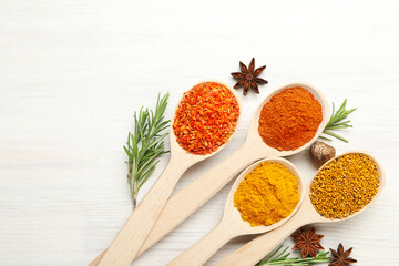 Different aromatic spices in spoons on white wooden table, flat lay. Space for text