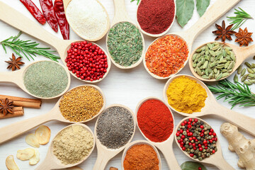 Different aromatic spices in spoons on white wooden table, flat lay