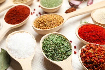 Different aromatic spices in spoons on white wooden table, closeup