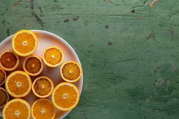 Freshly cut oranges and blood oranges resting on a pink plate on a green wooden table