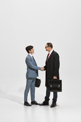 Two formally dressed men engage in handshake against white studio backdrop, representing new...