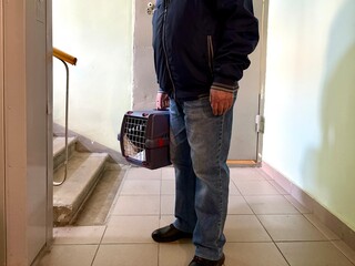 An elderly retired man holds a cat in a carrier. Pet transportation, traveling with a pet. A close friend of an elderly man