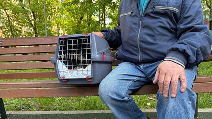 An elderly retired man holds a cat in a carrier. Pet transportation, traveling with a pet. A close friend of an elderly man