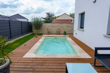 Piscine creusée avec rebords en carrelage, intégrée à une terrasse en bois moderne.