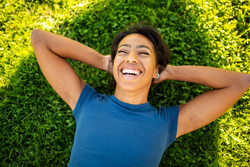 Smiling young woman lying on green grass with her hands behind her head