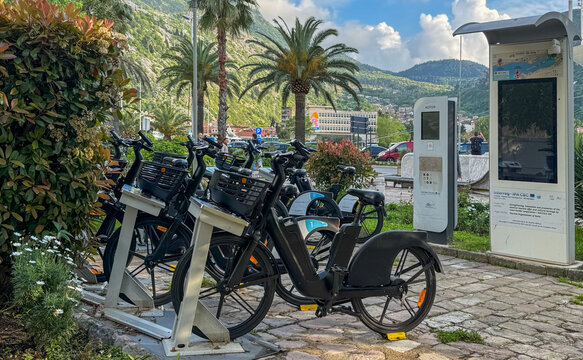 Kotor, Montenegro - April 25, 2025: Palm-lined bike-sharing station with parked GO2BIKE bicycles and info screens near the mountains and port of Kotor