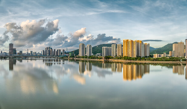Waterfront residential buildings with reflections on a calm lake under a cloudy sky at sunset in a coastal city.