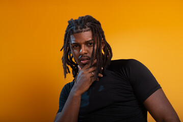 Studio portrait of handsome young man wearing black outfit and posing for photo against orange colored background. Confident and calm person.