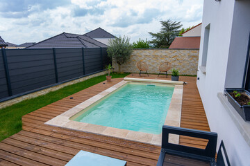 Piscine creusée avec rebords en carrelage, intégrée à une terrasse en bois moderne.