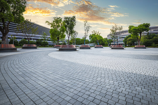 Empty brick paved plaza with trees and modern buildings in a business park area at dusk.