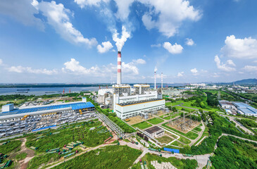 Large power plant with smoking chimneys and electrical substation by a river on a sunny day. Energy...
