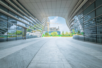 Perspective view from under a modern architectural archway towards contemporary glass buildings and green landscaping.