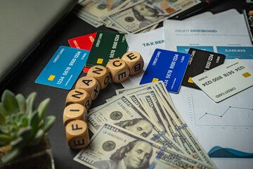 Flat lay of multiple credit cards, US dollar bills, financial reports, and wooden dice spelling ‘FINANCE’. Business and Finance background