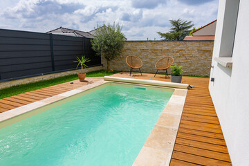 Vue d’ensemble d’une piscine aux rebords en carrelage, élégamment intégrée à une terrasse en bois dans un cadre extérieur moderne et apaisant.