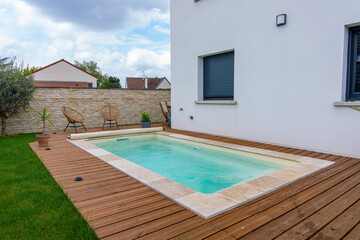 Piscine creusée avec rebords en carrelage, intégrée à une terrasse en bois moderne.