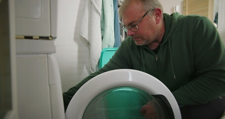 Man smiling while preparing to load laundry into a washing machine, with a laundry basket and...