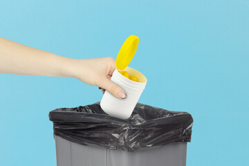 throwing plastic jar with vitamins into trash, outstretched hand with plastic jar with vitamins in front of trash can