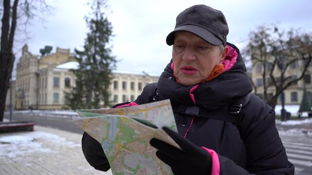 Elderly woman looks at a city map and plots a route. A grandmother is dressed warmly and walks in the park in winter. Grandma portrait. Talk