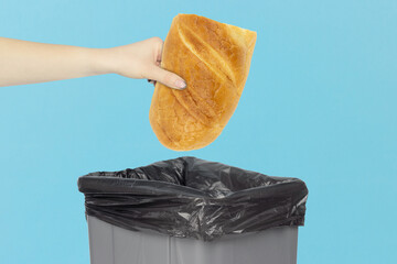 throwing loaf in the trash, outstretched hand with half of fresh bread in front of trash can,...
