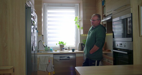 Man standing in modern kitchen, thoughtful pose, casual lifestyle, hands in pockets, serene home...