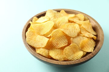 Tasty potato chips in bowl on light blue background, closeup
